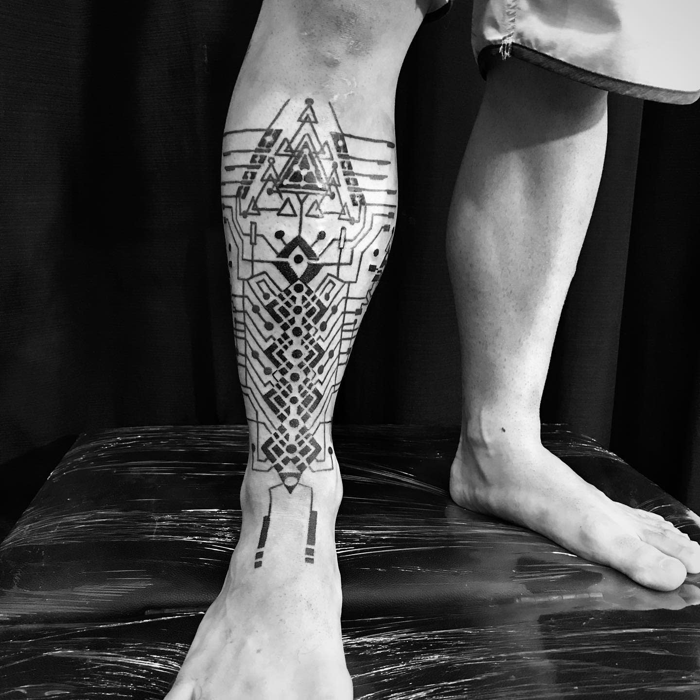 Complex cyberpunk tattoo on lower leg featuring geometric and circuit-inspired patterns with symmetrical lines